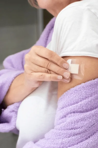 Close-up of a person's hand applying a clear hormonal medication patch to their upper arm in Henderson, NV.